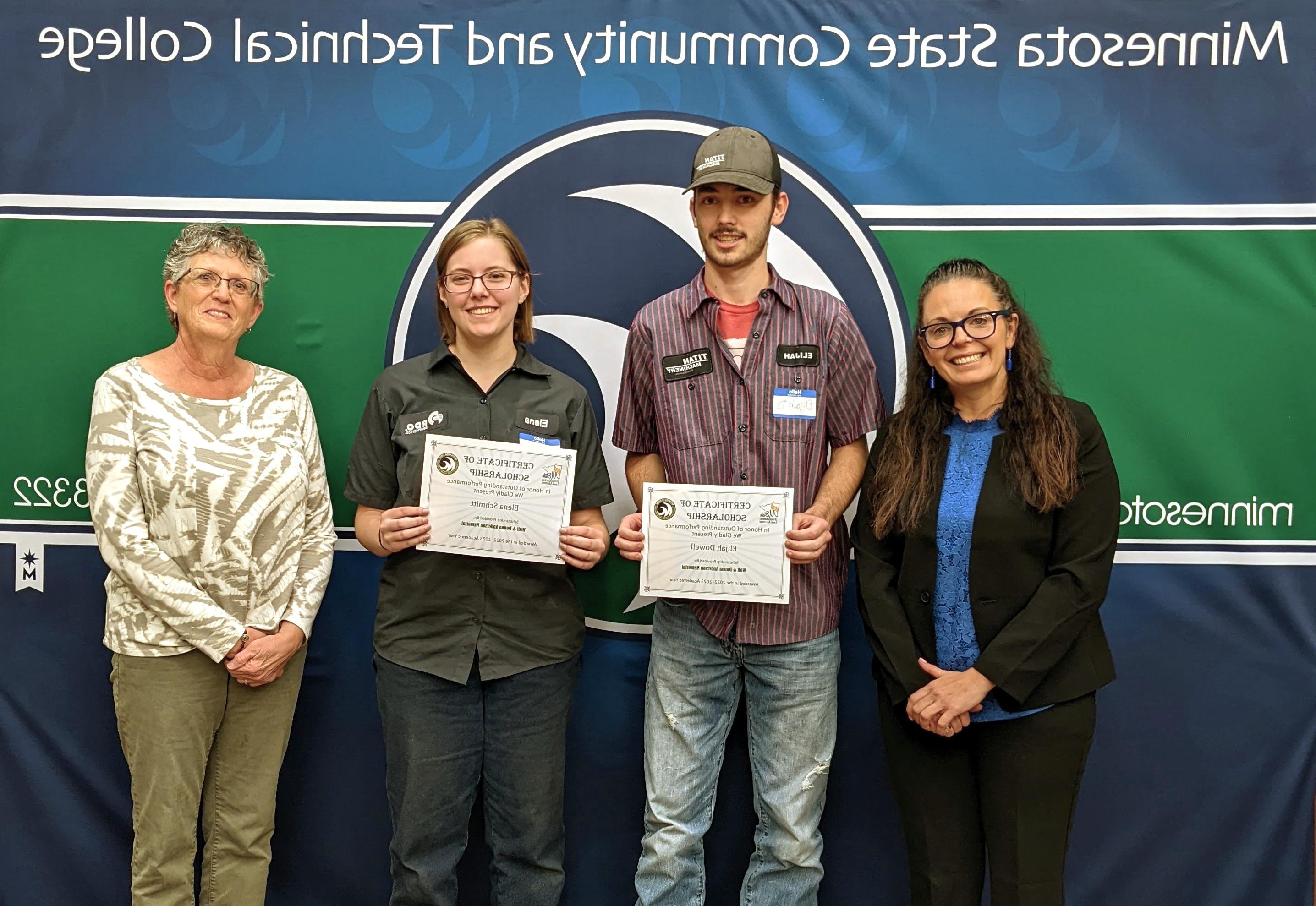 Four people, two holding certificates, stand in front of an M State banner