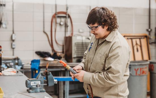 A student from the HVAC program is welding a copper pipe 